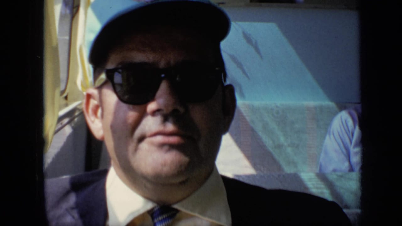 Man in sunglasses and cap seated beside a vehicle window.