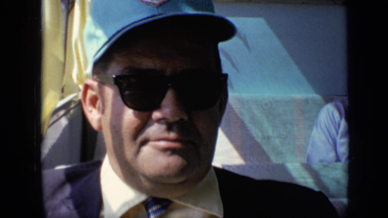 Man wearing sunglasses and a cap seated in a sunlit vehicle interior.