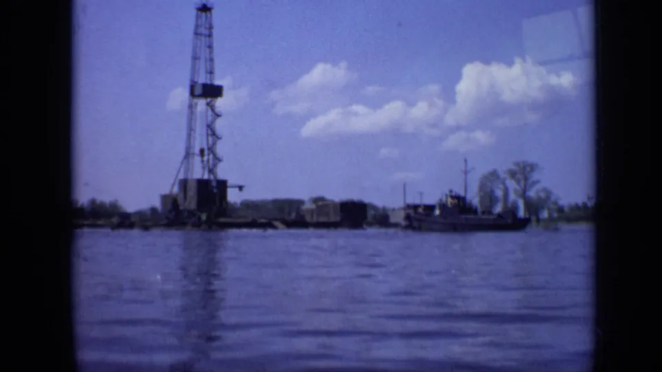 Color 8mm frame from Moscow in 1971 showing a tall derrick, shoreline equipment, water, and a small boat at the right edge.