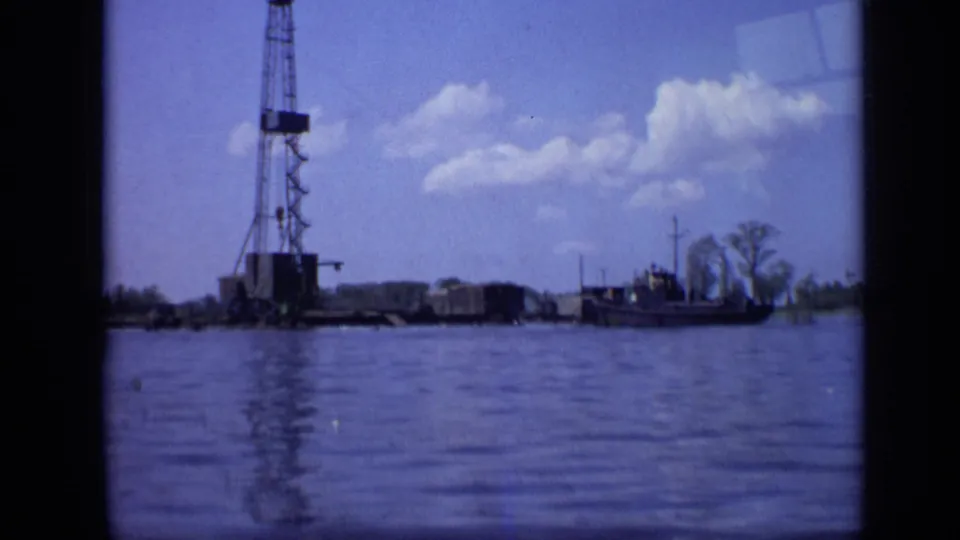 1971 8mm frame showing a Moscow waterfront derrick, rippled water, low industrial structures, and a small boat under a bright sky.