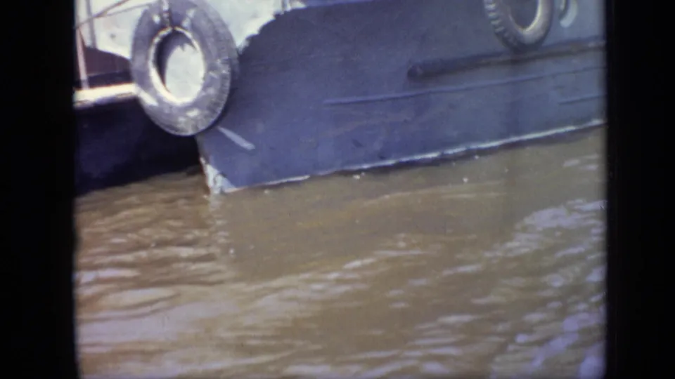 1971 8mm close-up of a dark boat hull, tire fender, and muddy water as the vessel passes or approaches dockside in Moscow.