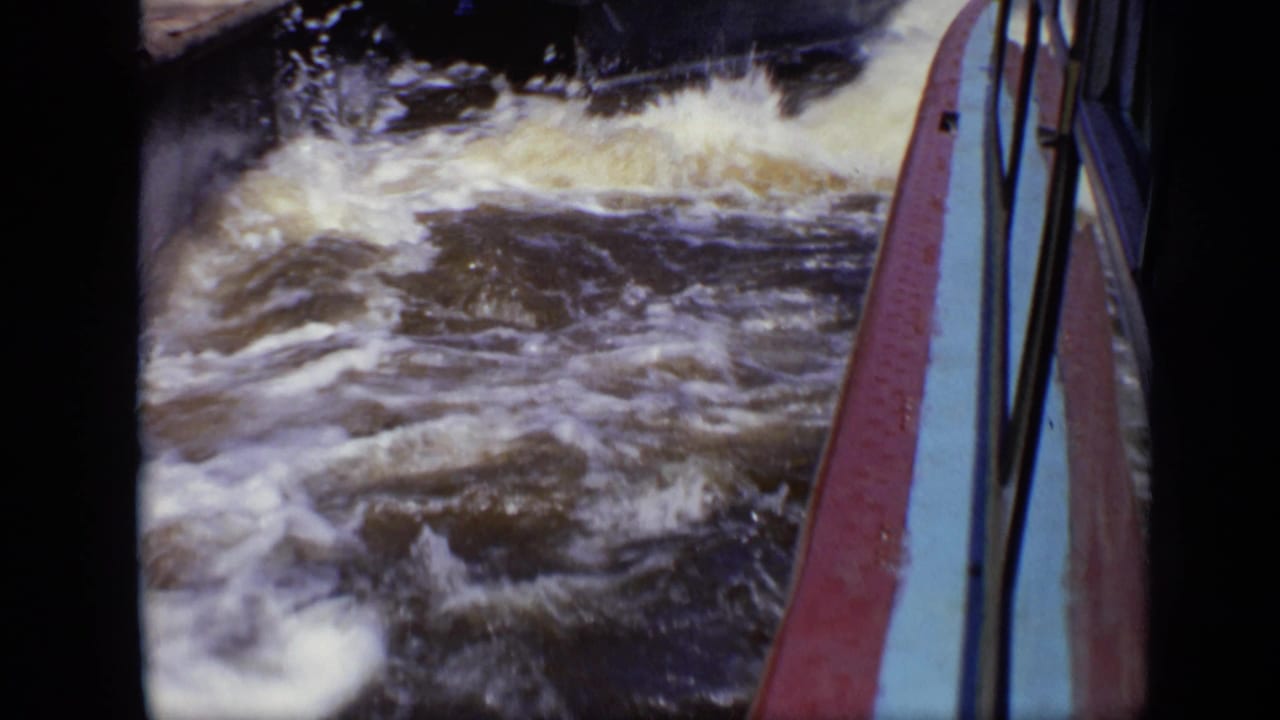 Churning water beside a boat with a red and blue rail in the foreground.