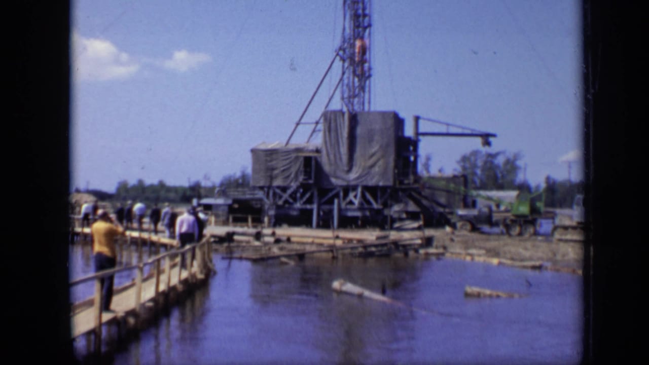 Adults continue along the pier in a 1971 Moscow industrial waterfront view with a rig platform, derrick and shoreline equipment.