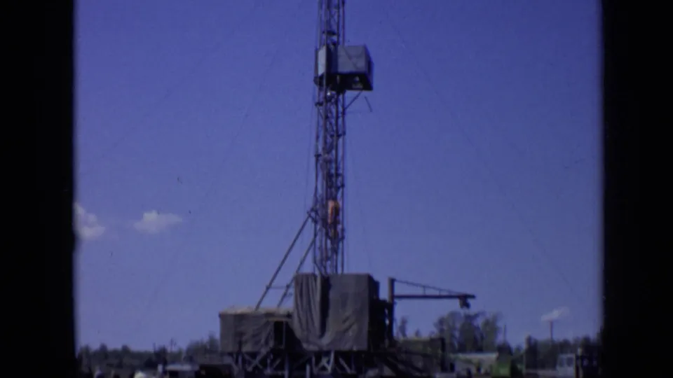 Final frame centers the derrick and tarped rig platform near water, with shoreline trees under a clear blue sky in 1971 Moscow footage.