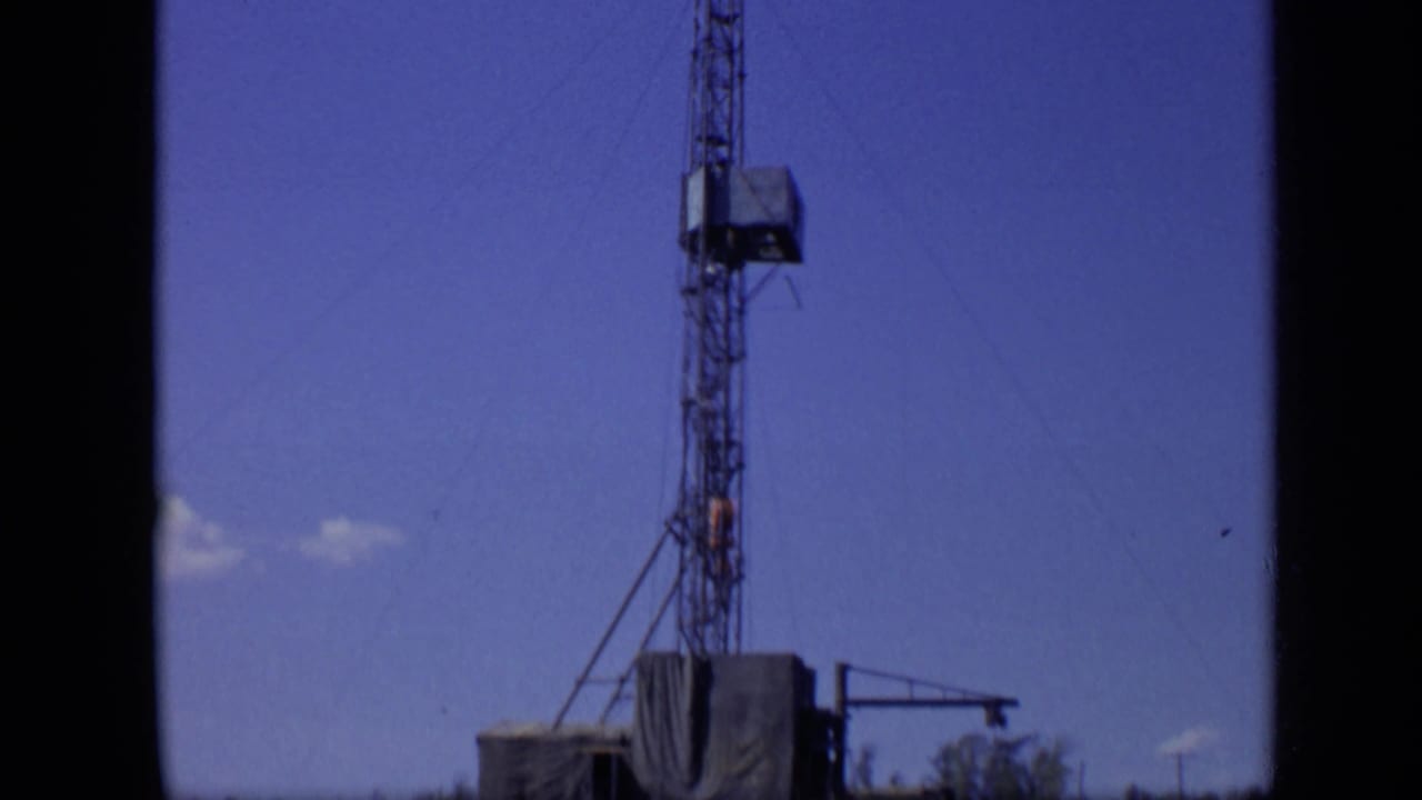 Lattice communications tower against blue sky near a riverside structure.