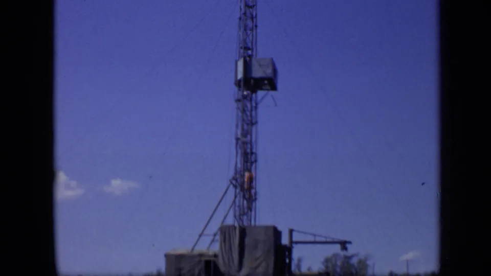 1971 Moscow home-movie frame showing a tall lattice tower above a low riverside structure under clear blue sky.