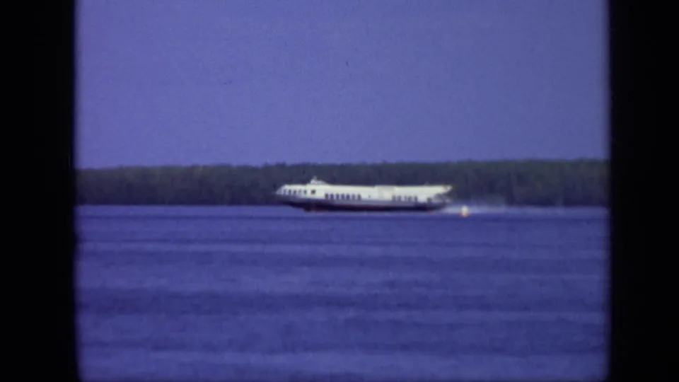 1971 Moscow 8mm frame showing a white passenger ferry crossing the river, with a small bright marker on the water and a wooded background.