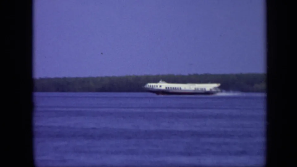 1971 Moscow frame of a white passenger ferry near the far side of a broad river, with wake spray and a dark wooded shoreline behind it.
