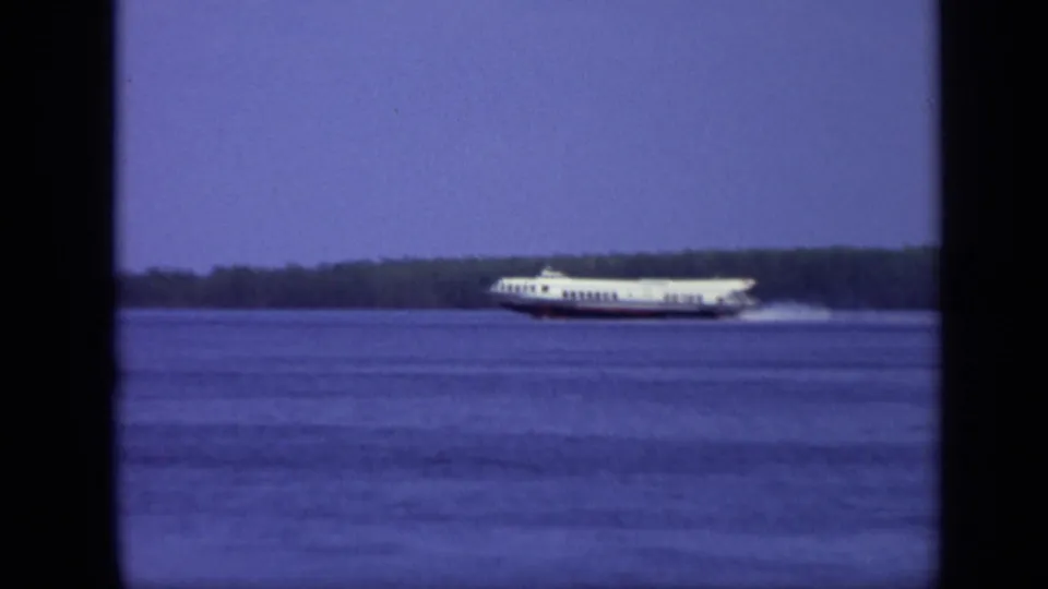The passenger ferry continues across the Moscow river scene, framed through dark film edges with the wooded shoreline in the distance.