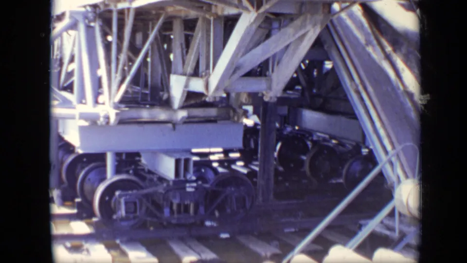 1971 Moscow 8mm frame showing heavy wheeled equipment under steel support beams near a river worksite.