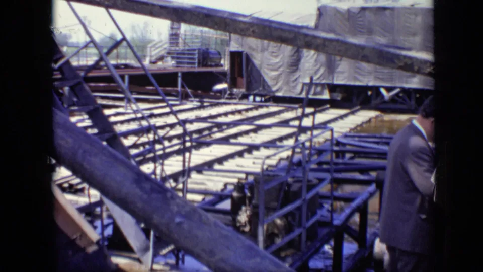 1971 Moscow 8mm frame showing a construction site with metal framing, wooden planks, covered equipment, and a partly visible suited man.