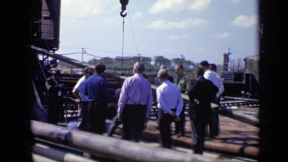 1971 Moscow 8mm frame showing several men gathered on a construction site with pipes, planking, a crane hook, and distant structures.