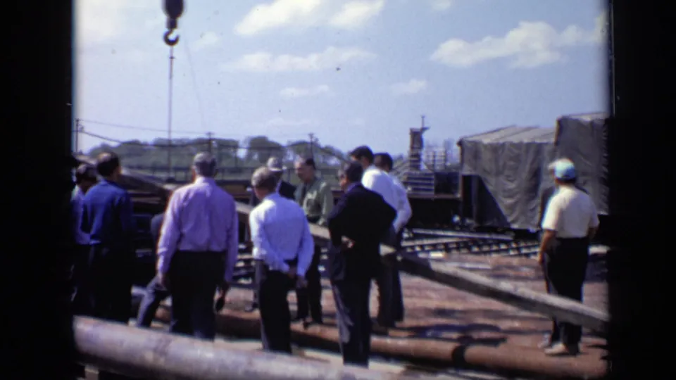 1971 Moscow 8mm frame showing a group of adult men surveying a construction site with pipes, scaffold elements, and covered equipment.