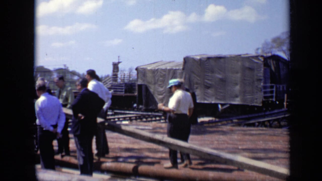 Adult men in work clothes and hard hats observe a covered freight car and tracks in 1971 Moscow home-movie footage.