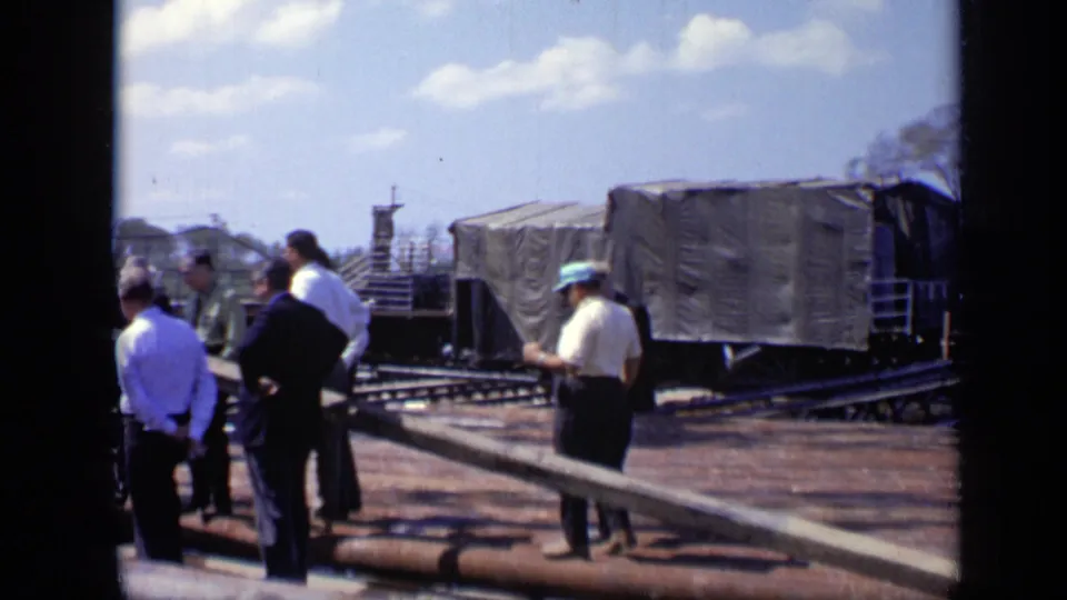 Adult men in work clothes and hard hats observe a covered freight car and tracks in 1971 Moscow home-movie footage.
