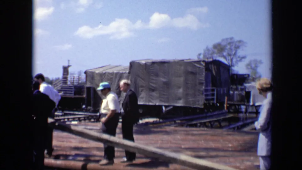 The 1971 Moscow scene shows men moving near a covered rail car, tracks, and long construction beams in bright daylight.