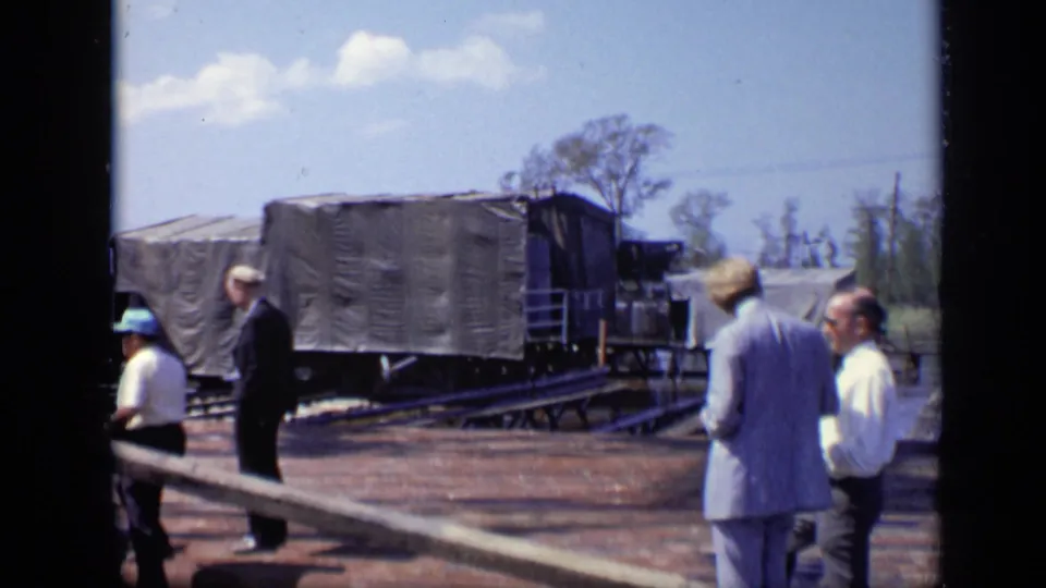 1971 Moscow home-movie frame showing men at an industrial construction site beside a covered structure, pipes, and open ground.