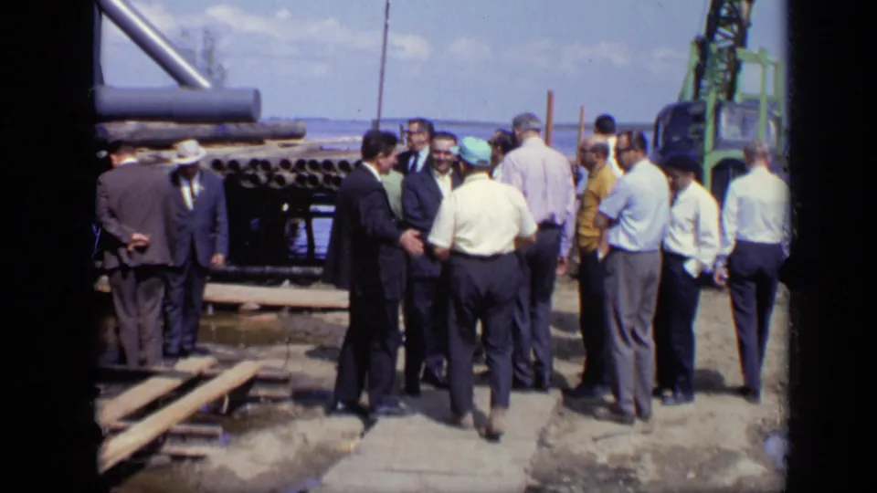 1971 Moscow frame with workers and suited visitors standing around pipes, planks, and equipment during an industrial site visit.