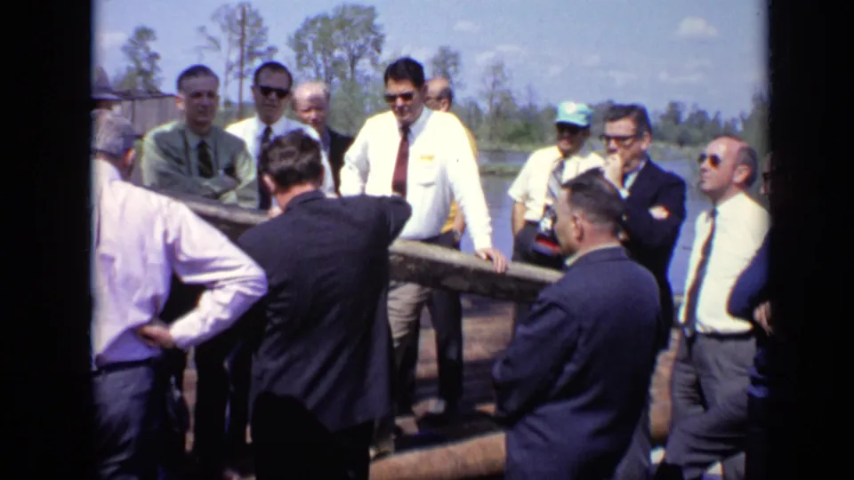 Close 1971 Moscow home-movie view of men in suits and work shirts gathered around a long pipe at an industrial site.