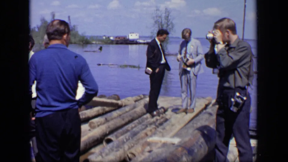 On the Moscow river raft, several men stand among logs while one man appears to take a photograph near the water.