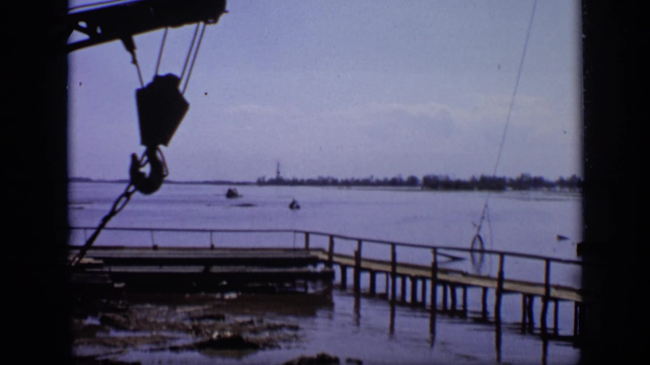 Crane hook and wooden pier beside a broad flooded shoreline.
