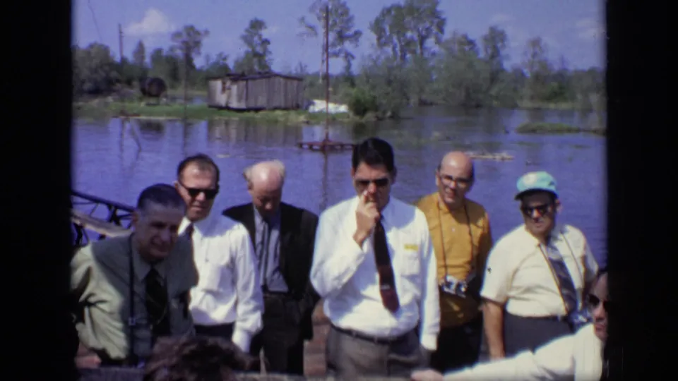 Several adult men on a pier face the camera and the flooded landscape behind them in 1971 Moscow home-movie footage.