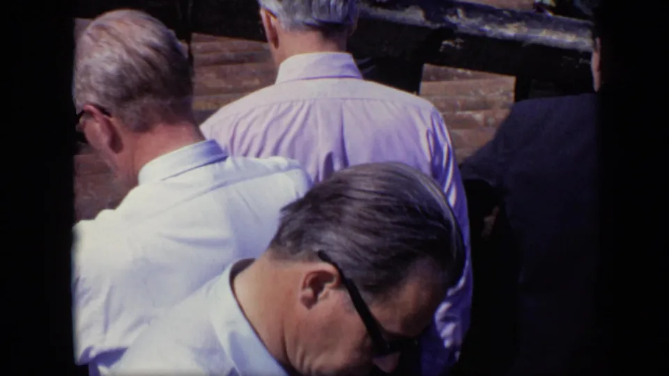Close 8mm view of adult men seen from behind on a pier, with one man in sunglasses leaning forward.