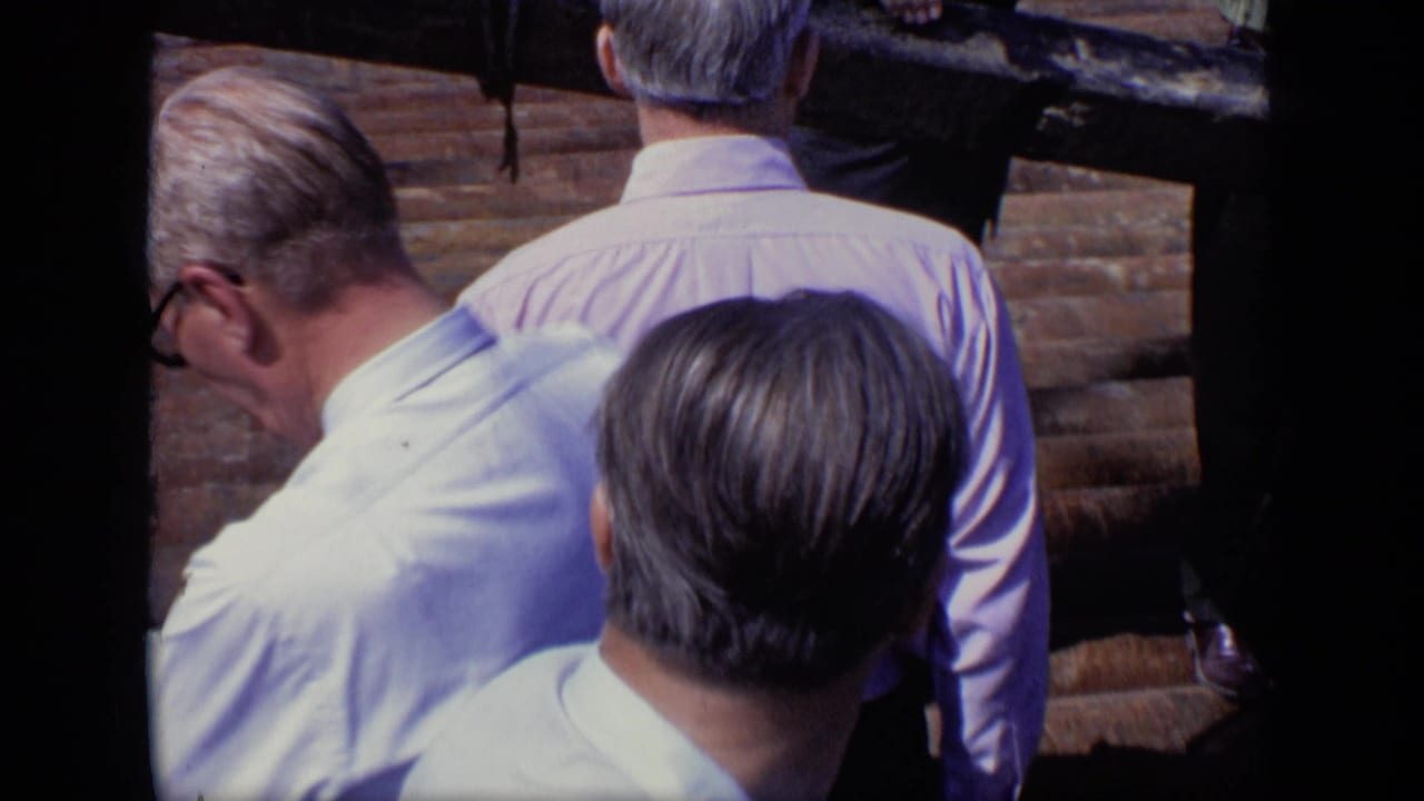 1971 Moscow home-movie frame showing adult men in pale shirts on outdoor steps, with one man in sunglasses looking downward.