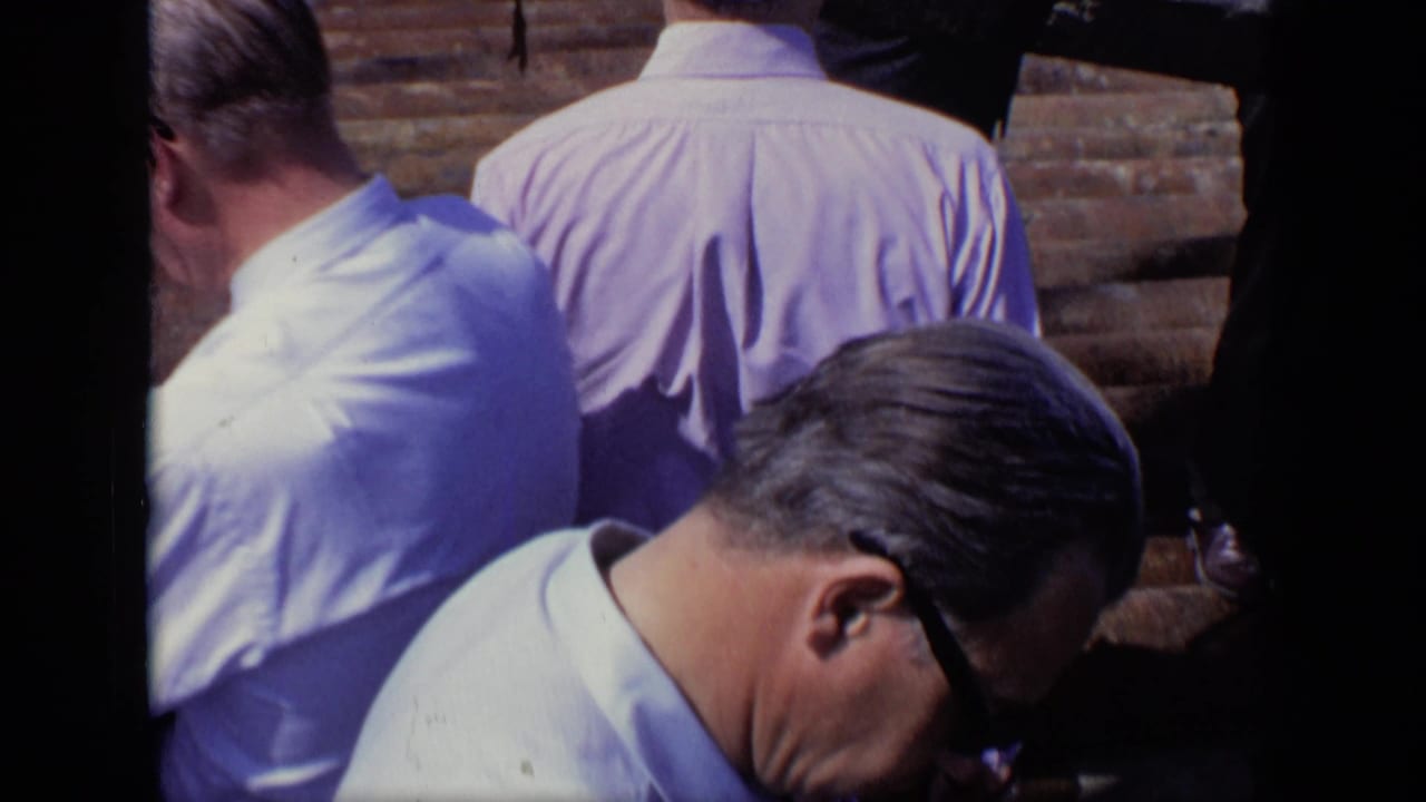 1971 Moscow home-movie frame of men in pale shirts seen from behind on steps, partly blocked by a dark vertical strip.