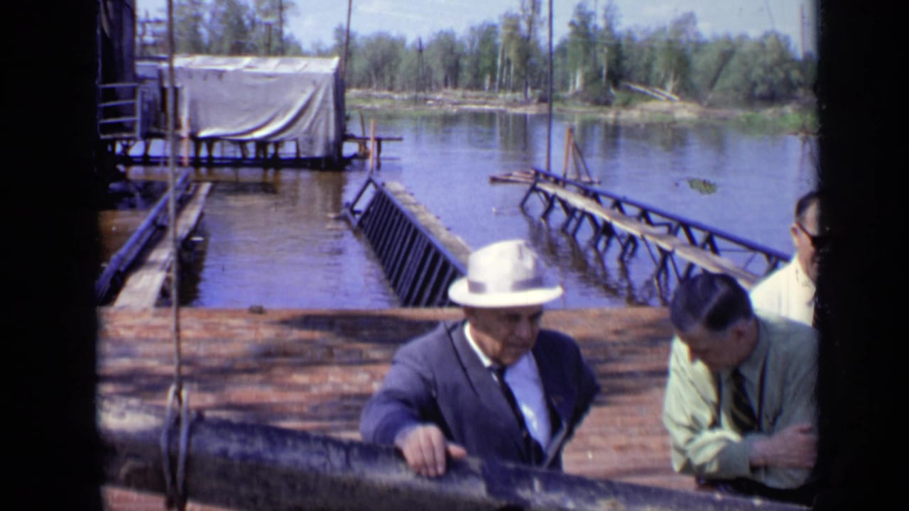 1971 Moscow 8mm frame showing suited men, including one in a white hat, near a wooden lakeside railing and dock structure.
