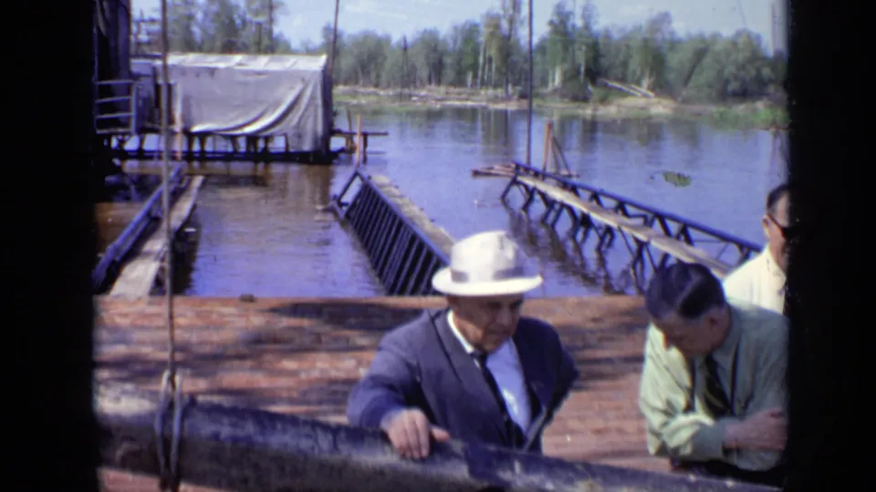 1971 Moscow 8mm frame showing suited men, including one in a white hat, near a wooden lakeside railing and dock structure.