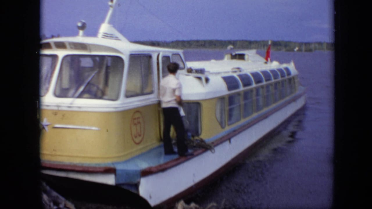 Yellow and white passenger boat docked on the water with a person standing near the cabin.