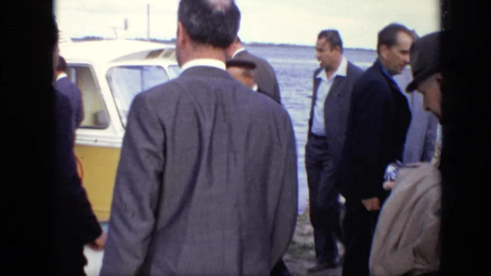 Formally dressed men gather beside a yellow passenger boat at a Moscow waterfront in 1971, viewed from close handheld footage.