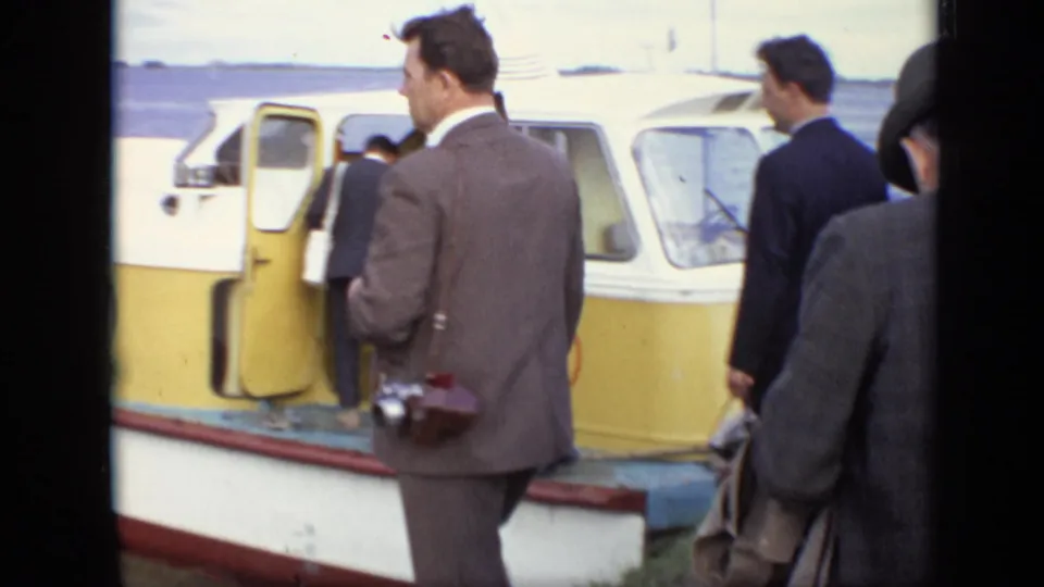 At the Moscow dock, a suited man with a still camera watches while other adults board the yellow passenger boat.