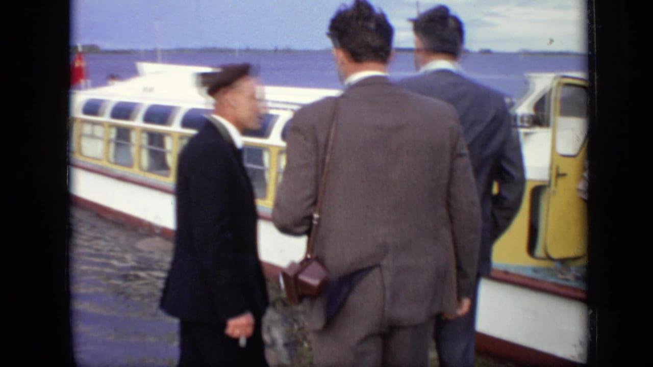 In 1971 Moscow, suited men and a uniformed man stand near the open doorway of a yellow passenger boat by the water.