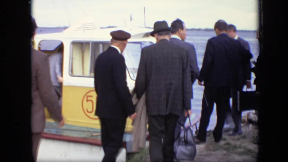 At the Moscow waterfront, men in business dress carry briefcases and bags beside the yellow passenger boat during boarding.