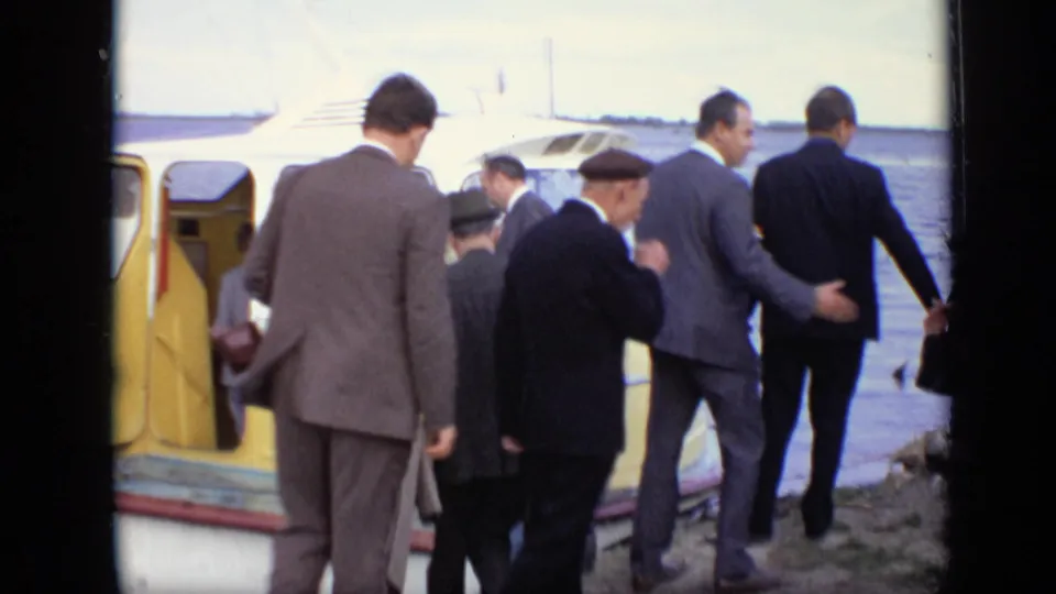 Suited men pass the open door of the yellow passenger boat in Moscow, with water and the dock visible behind them.