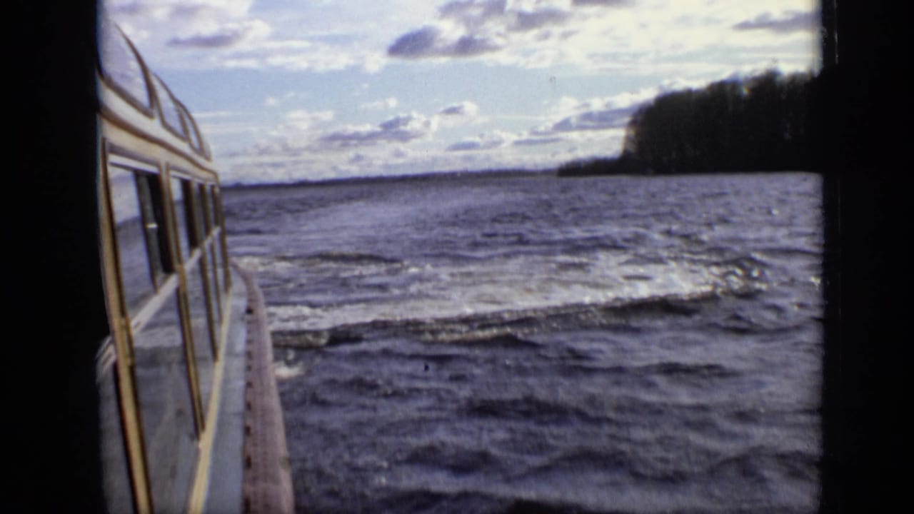 1971 8mm Moscow lake footage shows the side of a yellow-and-white boat moving past rippling water and a wooded shore.