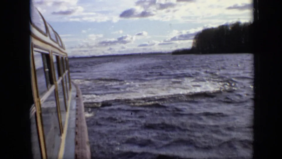 1971 8mm Moscow lake footage shows the side of a yellow-and-white boat moving past rippling water and a wooded shore.