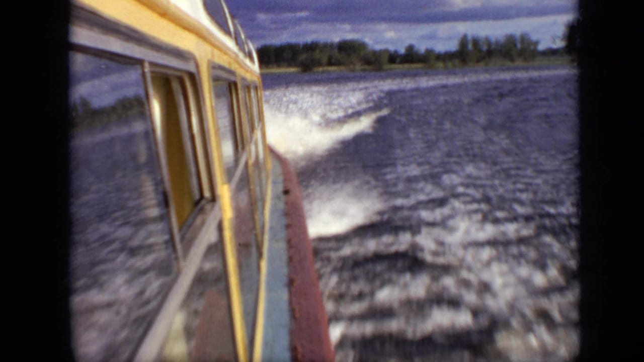 Yellow boat side moving across a river with white wake and wooded shoreline.