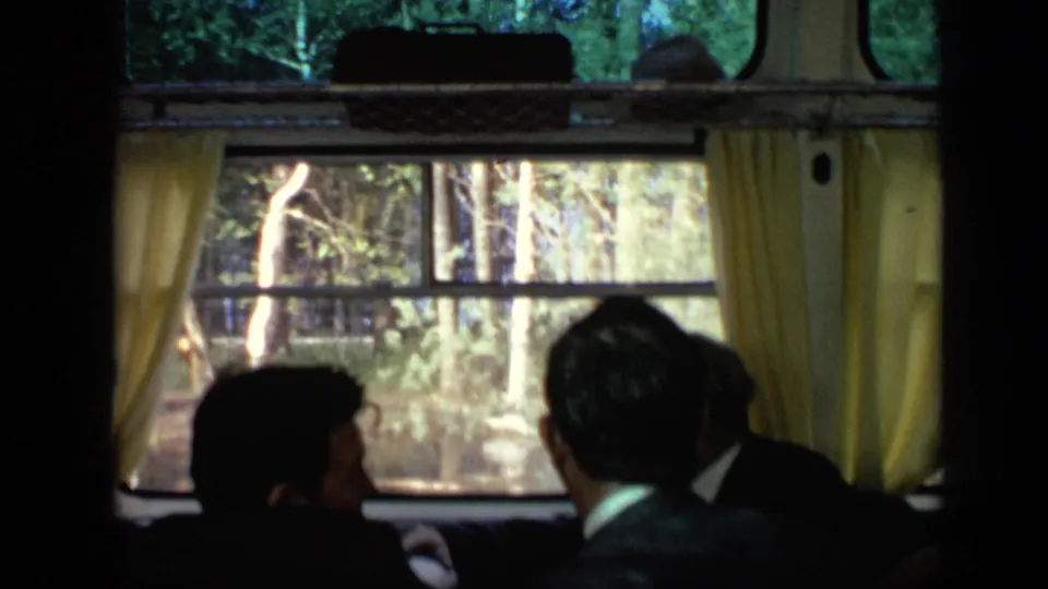 Passengers in dark clothing look through curtained cabin windows at a forested bank during a 1971 Moscow river trip.