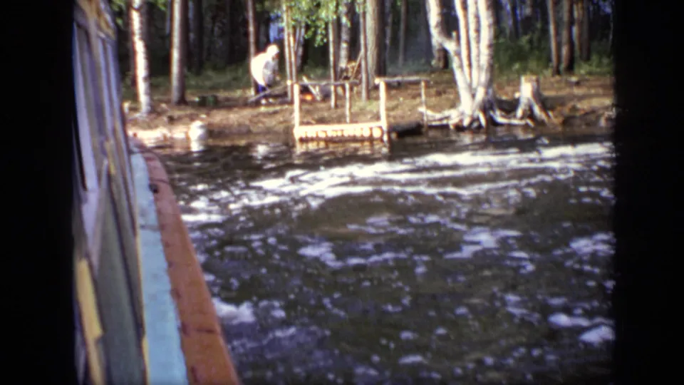 From the boat side, a small wooded landing appears along the riverbank, with a person near simple wooden structures.