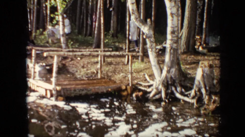 1971 Moscow 8mm frame showing the dock and water from a handheld angle, with a light-clothed figure partly obscured by trees.