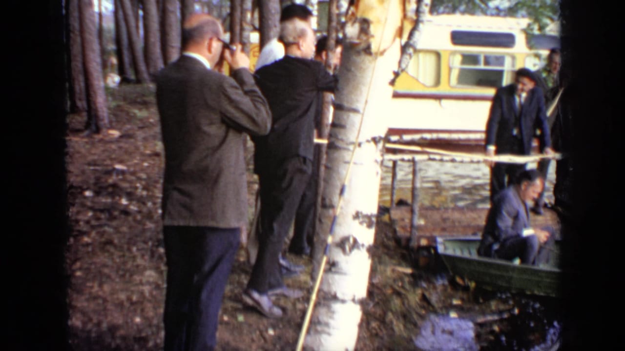 1971 Moscow 8mm frame with men in suits at a birch trunk, a man by a small boat, and a bus parked beyond the trees.