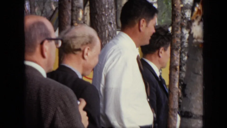 Older men in suits stand and talk near birch trees and a yellow bus in Moscow, based on 1971 clip metadata.