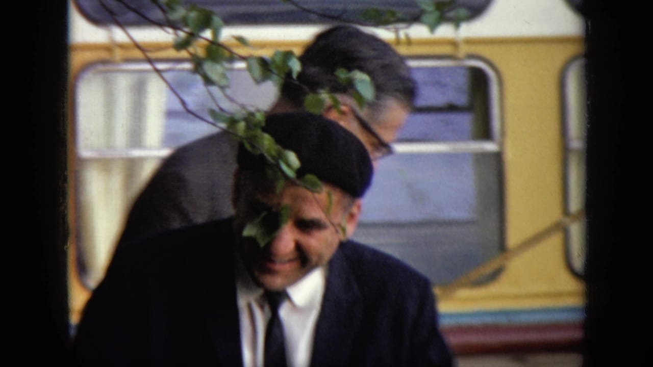 A man in a black beret passes in front of a yellow bus.