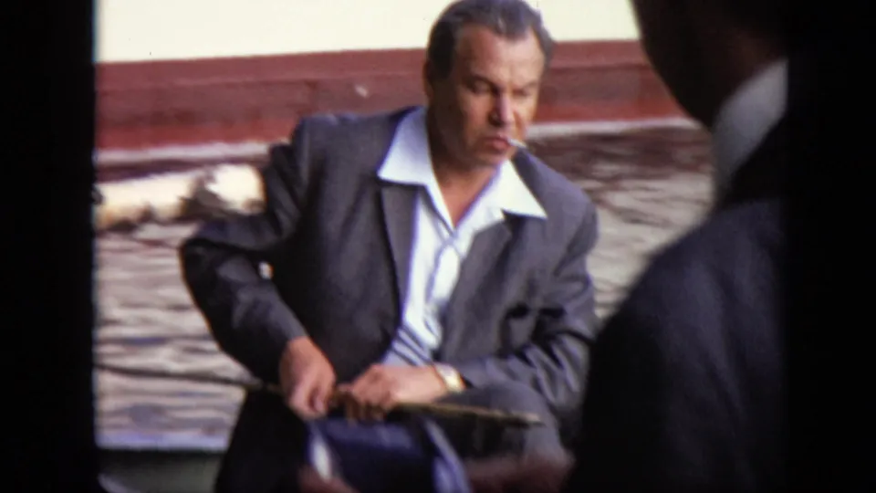 Adult man in a dark suit and open white shirt smokes while seated in a rowboat in 1971 Moscow footage.