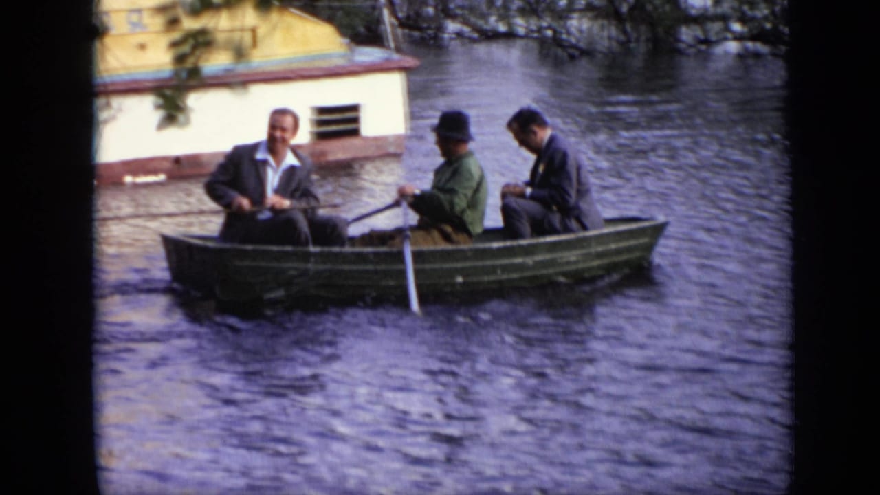 In this 1971 Moscow frame, one man rows while two other adult men sit in a small green boat on a calm river.