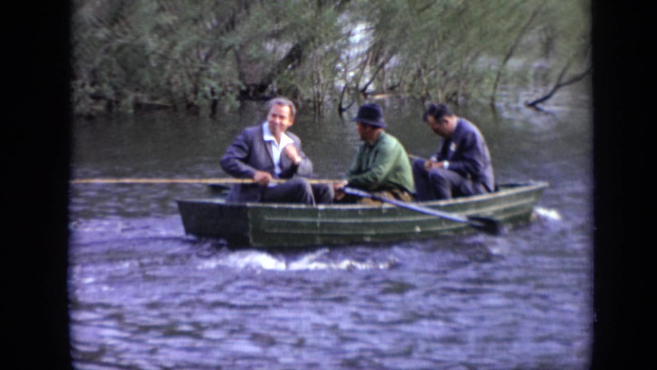 A man rows while two other men sit in a small boat on the water.