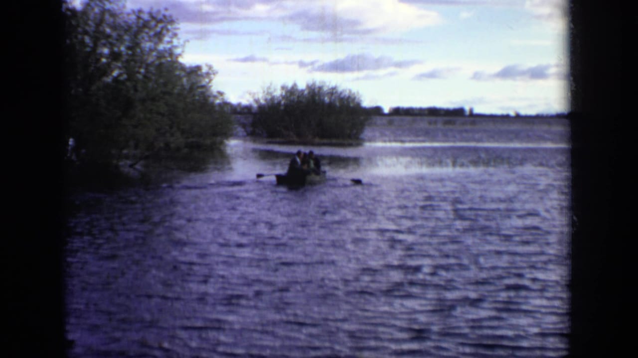 Several people appear in a small rowboat on a Moscow lake, framed by trees and dark 8mm film edges.